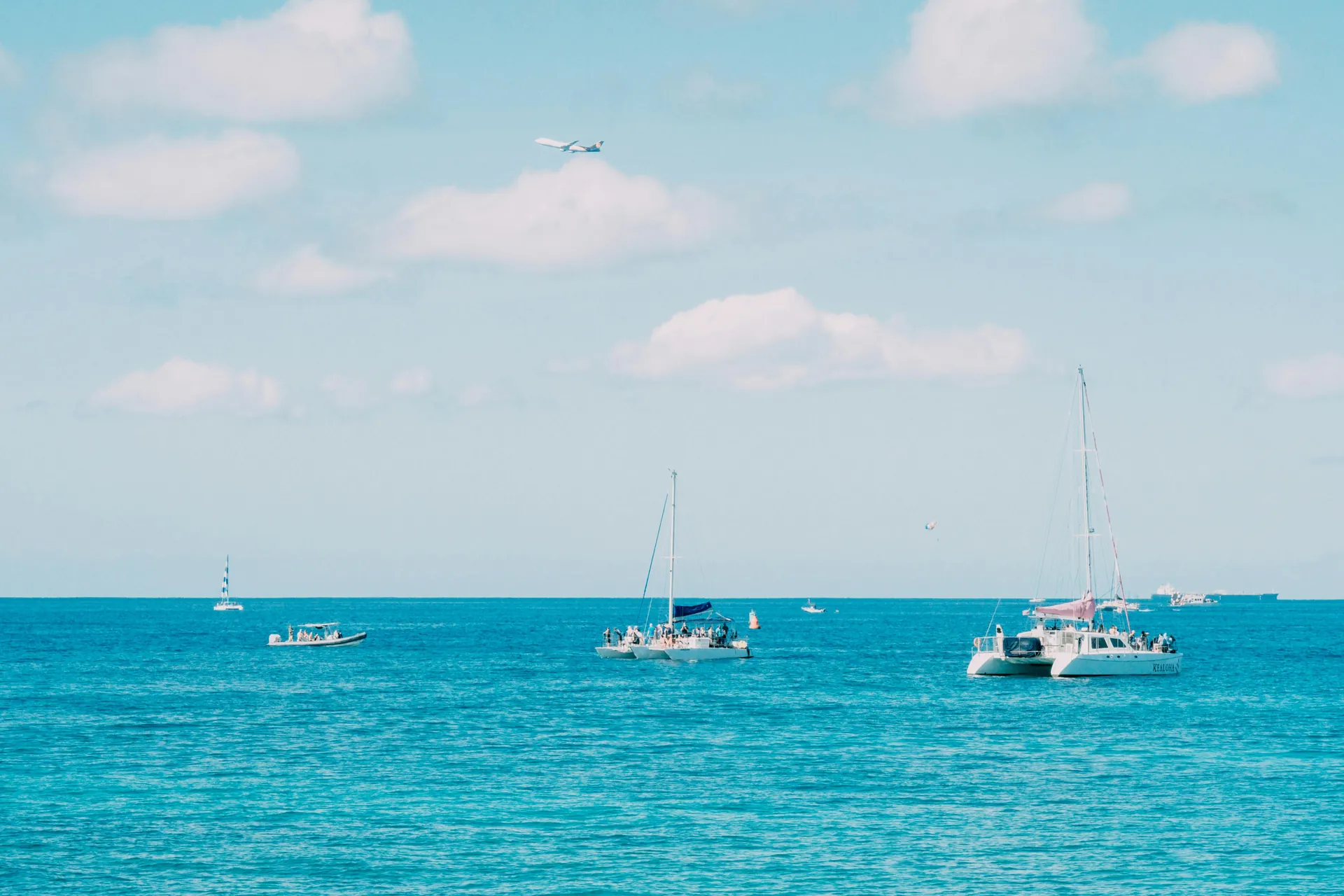 Beautiful ocean view with catamarans and an airplane against blue skies.