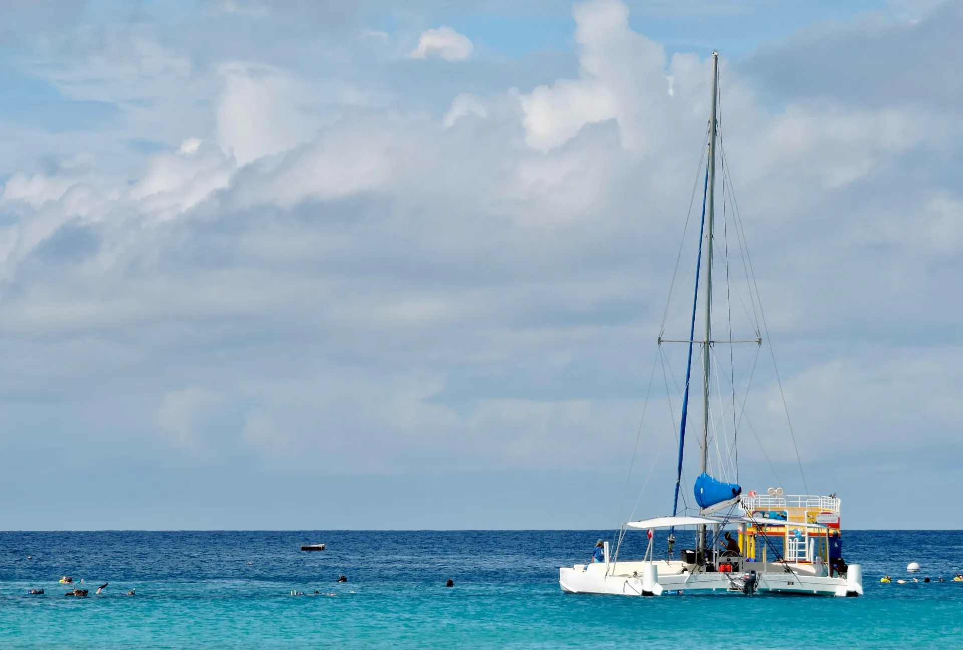 A catamaran floats on turquoise Caribbean sea under a cloudy sky in Barbados.